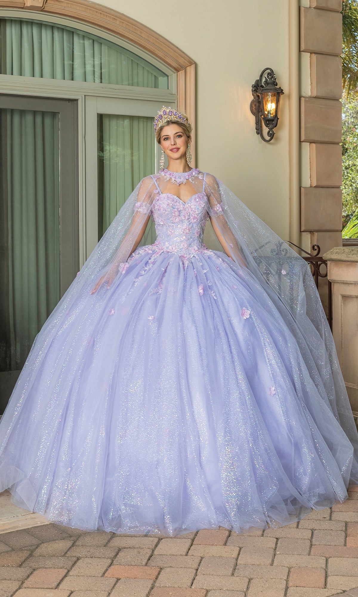Young woman in Quinceanera Dress 1785 By Dancing Queen—a lilac ball gown with sweetheart neckline and tiara—stands outdoors on a stone patio before a large window and ornate doorway.
